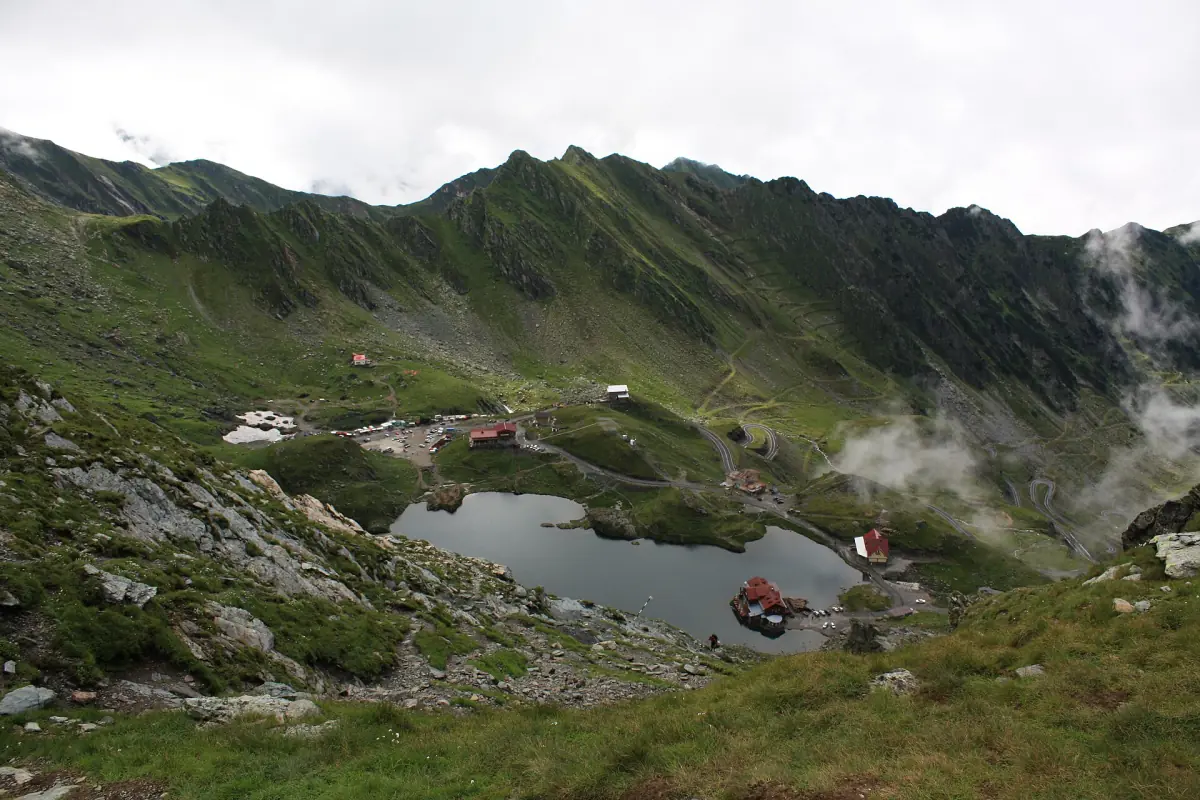 Bâlea Lake seen from above in a green mountain bowl with mist on the ridges