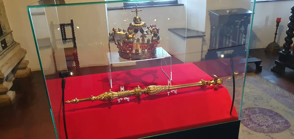 Golden crown and sceptre on red velvet in a glass display case