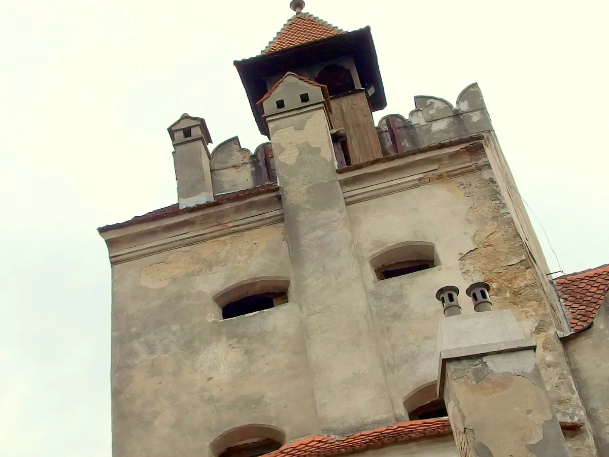 Castle tower with a small pointed roof and chimneys against a pale sky