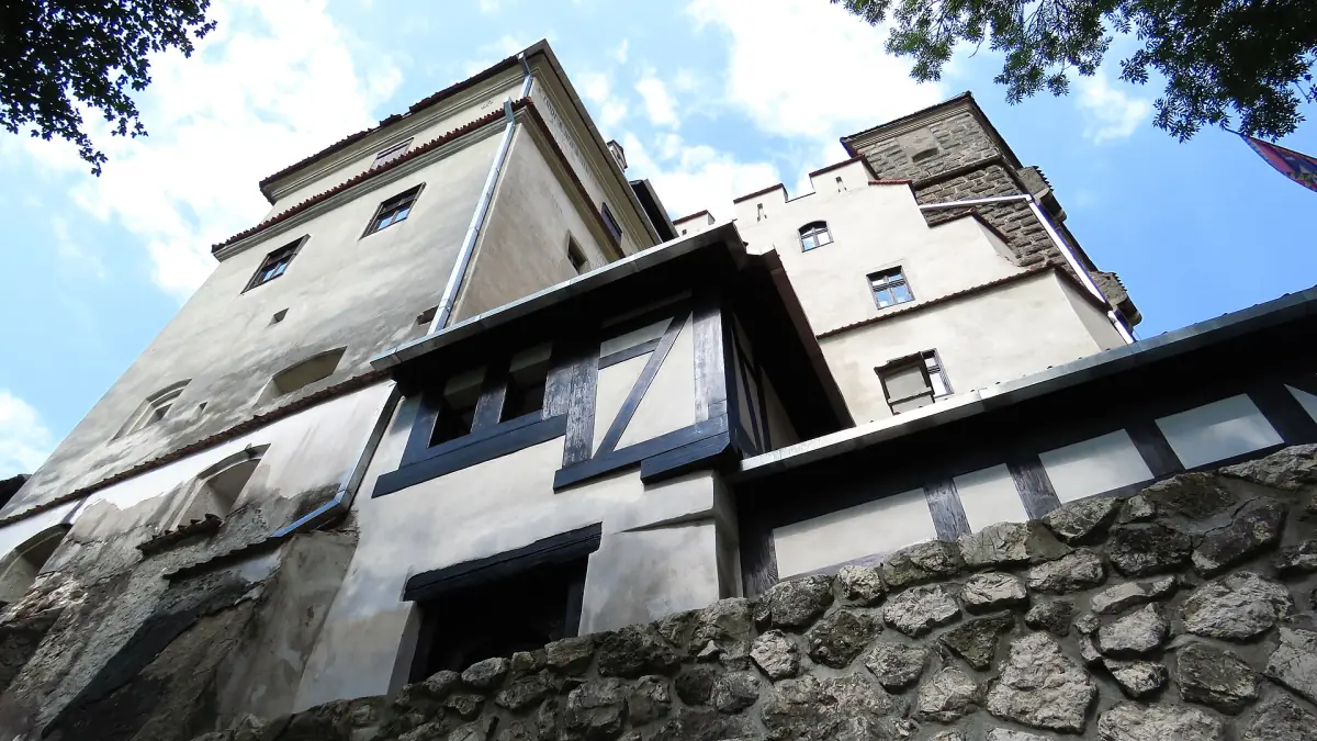 White castle walls and windows rising above a stone base, seen from below