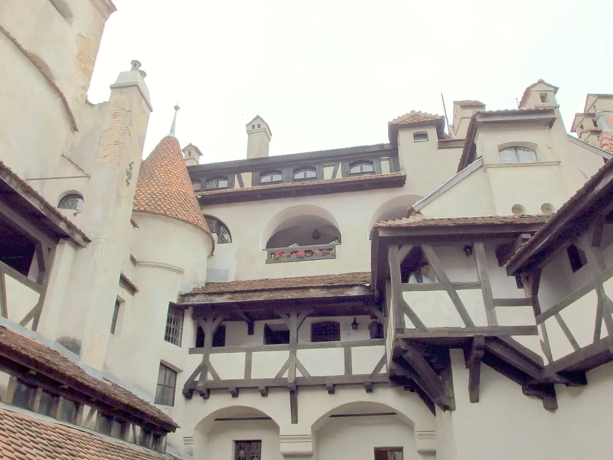 Bran Castle seen from its courtyard, with white walls, a conical turret and timber galleries under a pale daylight sky