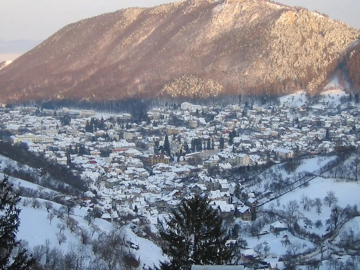 Snow covered rooftops of Brașov in front of a sunlit mountain