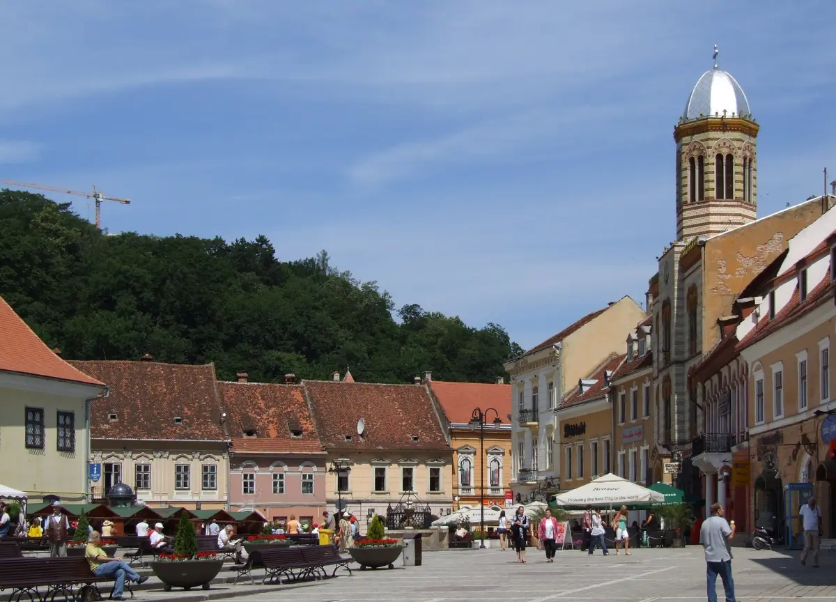 Pedestrian street in the old town of Brașov with a church dome and wooded hill