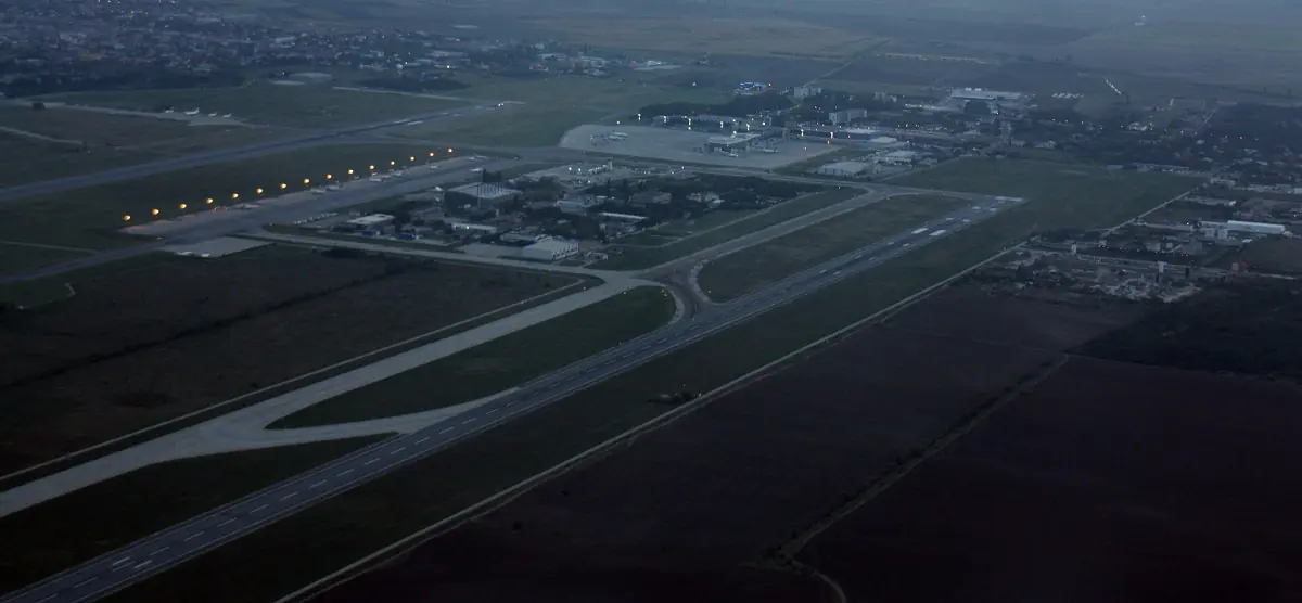 Aerial view of an airport at dusk with lit runways and taxiways beside dark fields