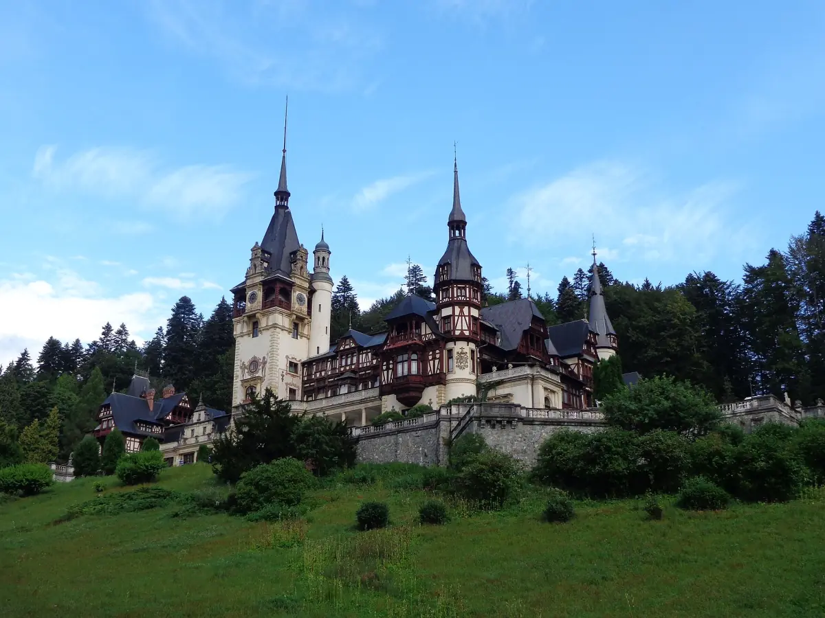 Peleș Castle with many towers set among green lawns and fir forest